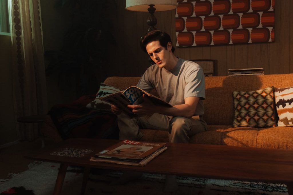 A man reading a book on a retro sofa in a warm, lamp-lit room — the ideal setting for working through a ranked reading list