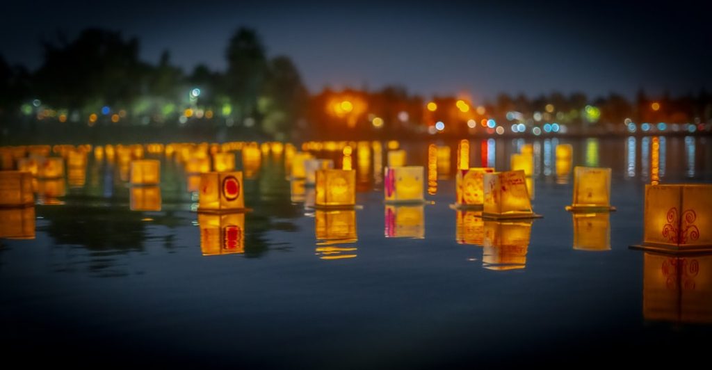 Glowing paper lanterns floating on dark water at a night festival, their warm light reflecting on the surface